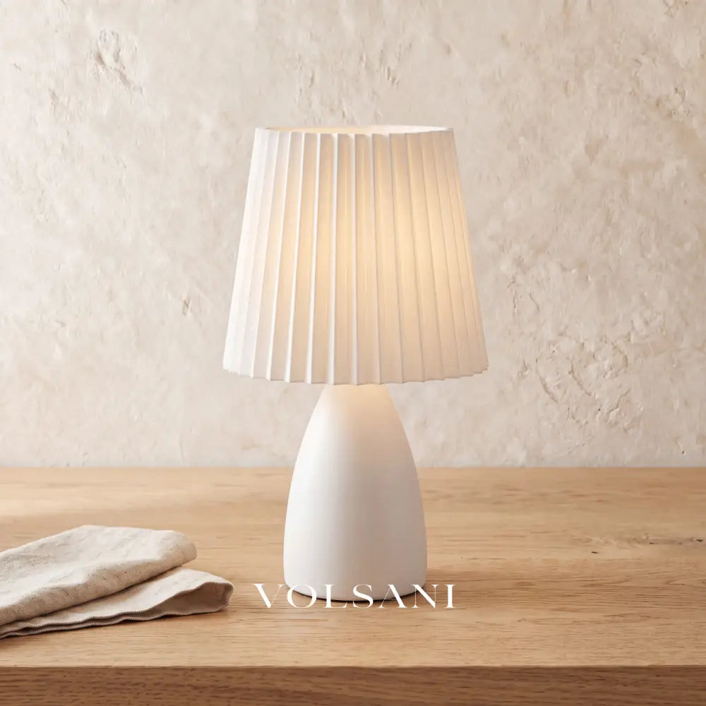 Close-up of the white ceramic pleated-shade lamp on raw oak against a plaster wall