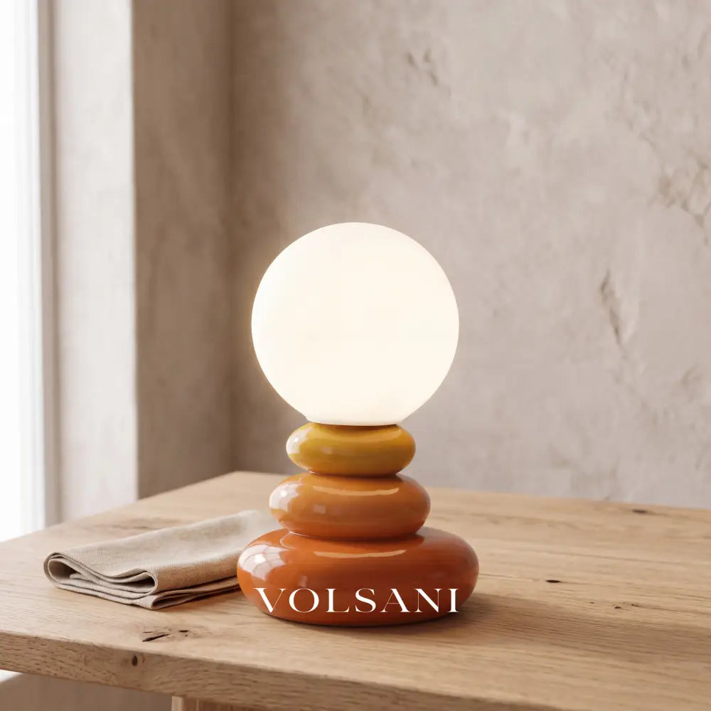 Close-up of the orange stacked ceramic lamp on raw oak against a plaster wall