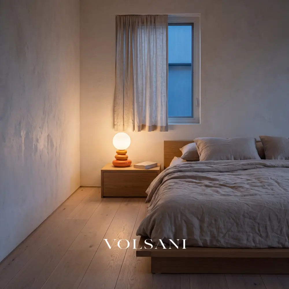 Orange stacked ceramic lamp lit on a bedside table in a Japandi bedroom at dusk