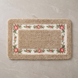 Sand Blossom floral border bath mat, overhead on stone floor