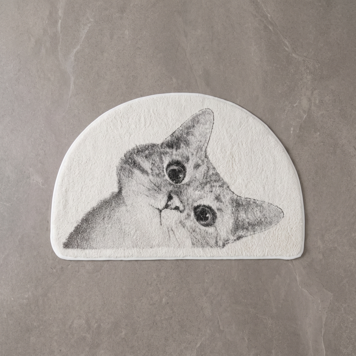 Curious Kitty cat bath mat on a pale stone floor, overhead