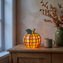 Stained glass pumpkin lamp glowing on an oak sideboard