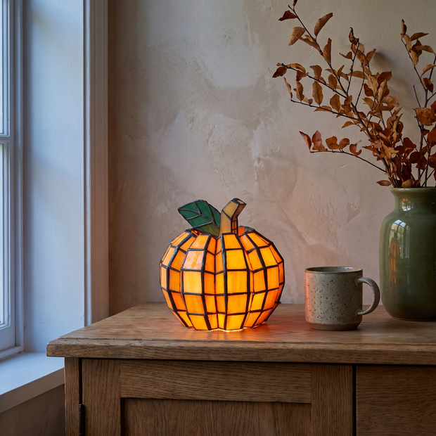 Stained glass pumpkin lamp glowing on an oak sideboard
