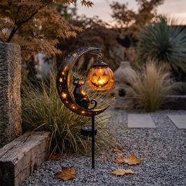 Solar cat and moon garden stake glowing in a garden bed