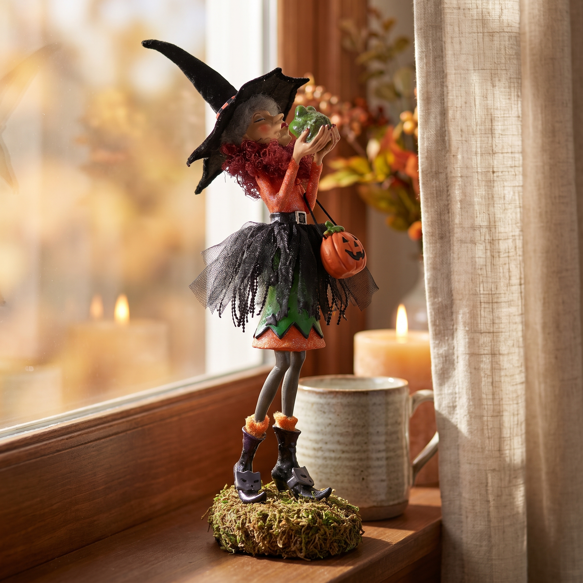 Clarice witch figurine close-up on a windowsill beside a candle