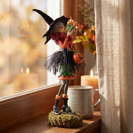 Clarice witch figurine close-up on a windowsill beside a candle