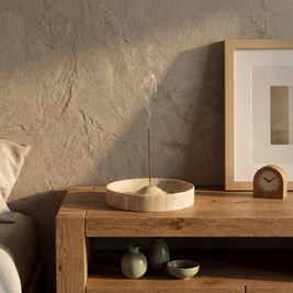 Beige stone incense holder with lit incense on an oak bedside table