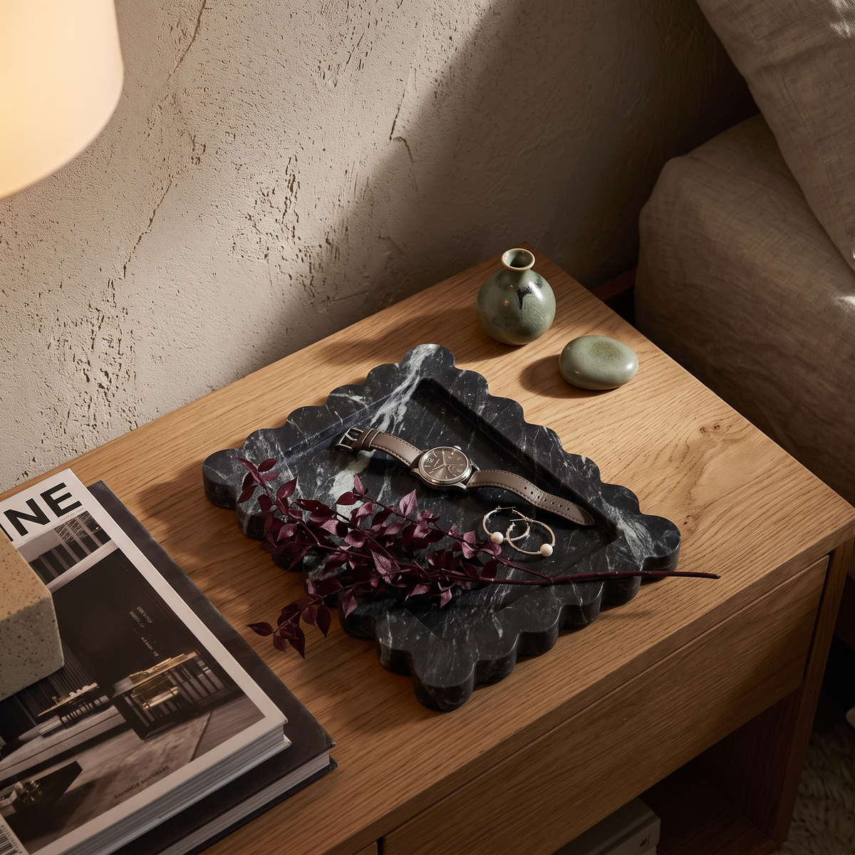 Black scalloped marble tray with a watch on a bedside table
