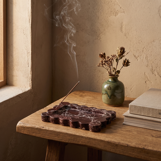 Burgundy scalloped marble tray with lit incense on a side table