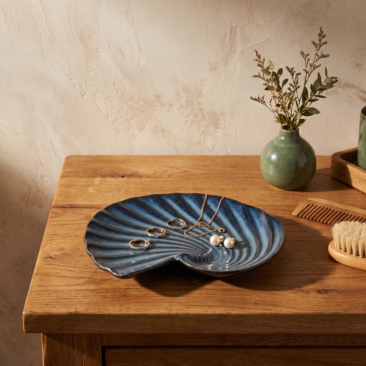 Deep blue porcelain shell plate holding gold jewelry on a dressing table