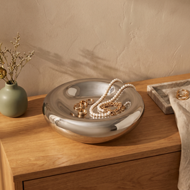 Silver glass saucer bowl holding gold and pearl jewelry on an oak dresser
