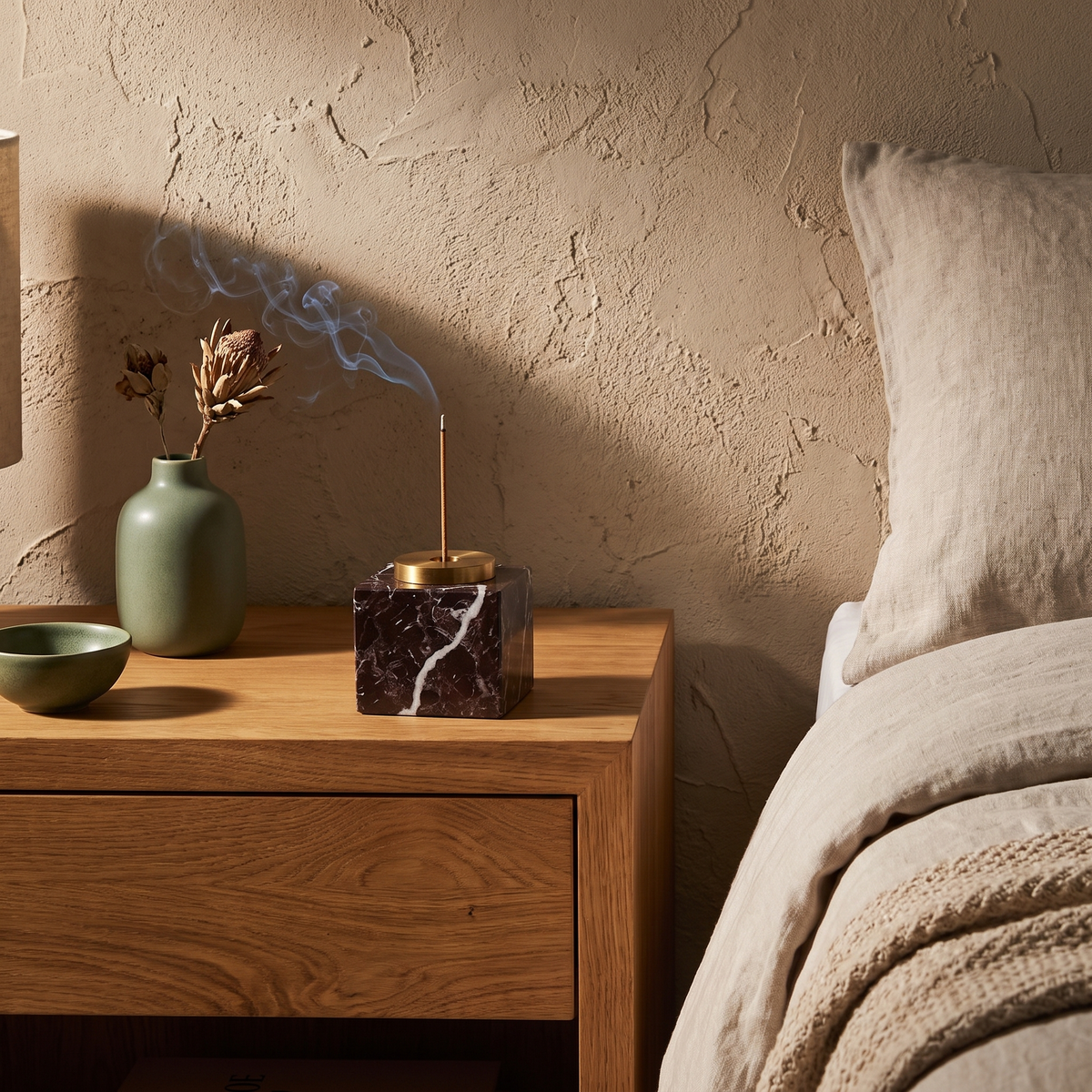 Square dark brown marble incense holder with lit incense on a bedside table