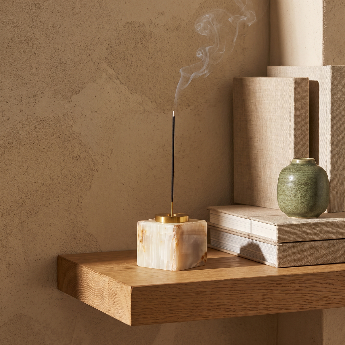 Square natural marble incense holder with lit incense on an oak shelf