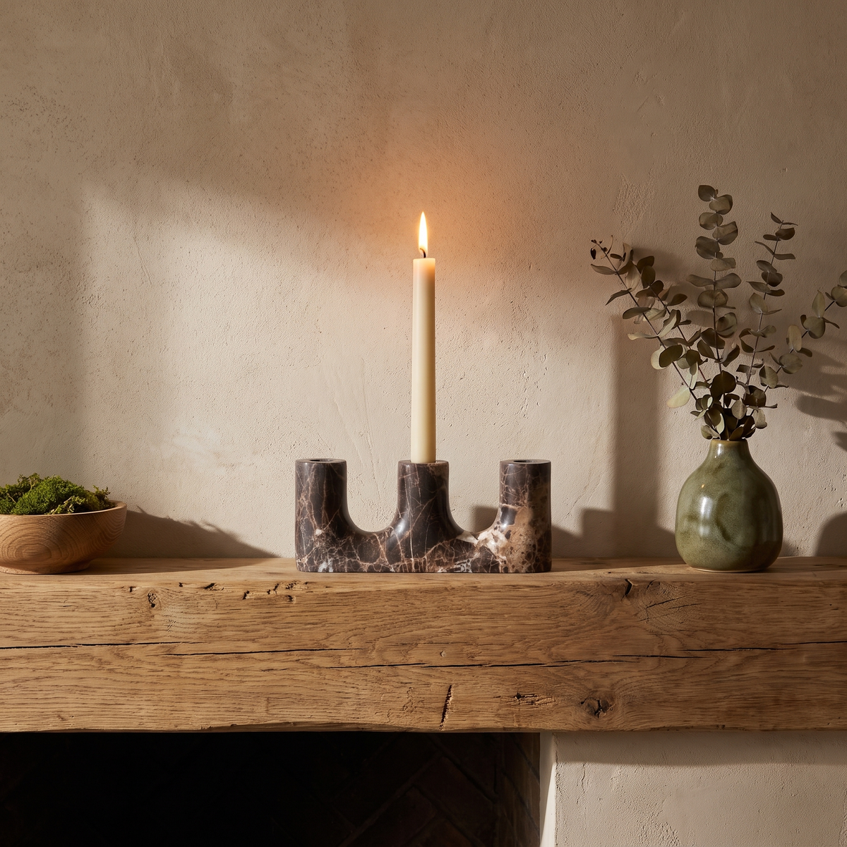 Brown stone candle holder with a lit taper on a fireplace mantel