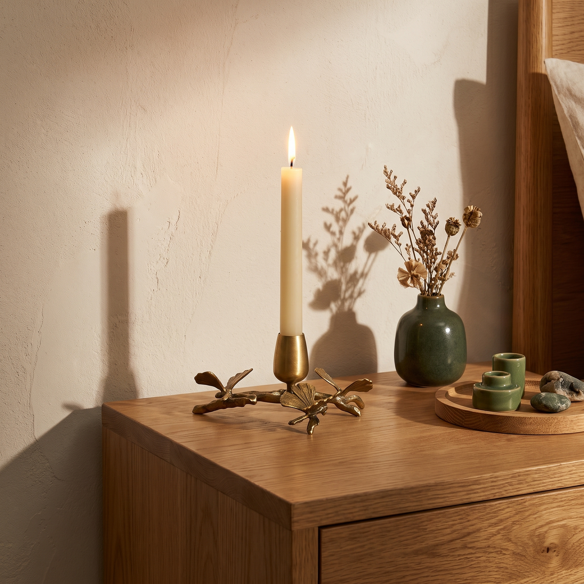 Brass ginkgo candle holder with a lit taper on a bedside table