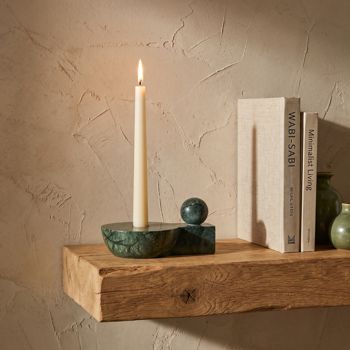Green marble taper candle holder with sphere styled on an oak shelf beside two books
