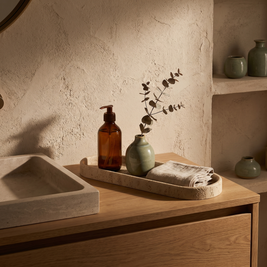 Long oval sandstone vanity tray styled on a bathroom vanity counter behind the sink