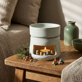 Ceramic tealight oil diffuser and wax warmer close-up, on an oak side table with a tealight glowing inside