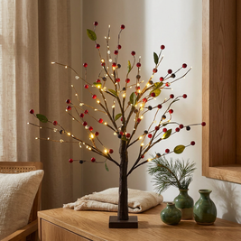 Red berries lighted tabletop twig tree with LEDs close-up, on an oak console table, lights glowing