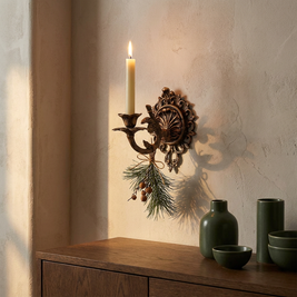 Vintage iron scrollwork wall candle sconce close-up, mounted on a plaster wall above an oak console, holding a taper candle