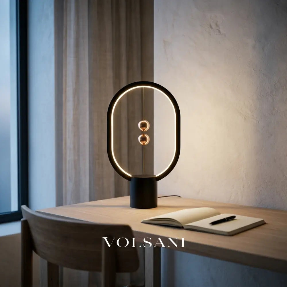 Black magnetic sphere lamp lit on an oak desk at dusk, medium view