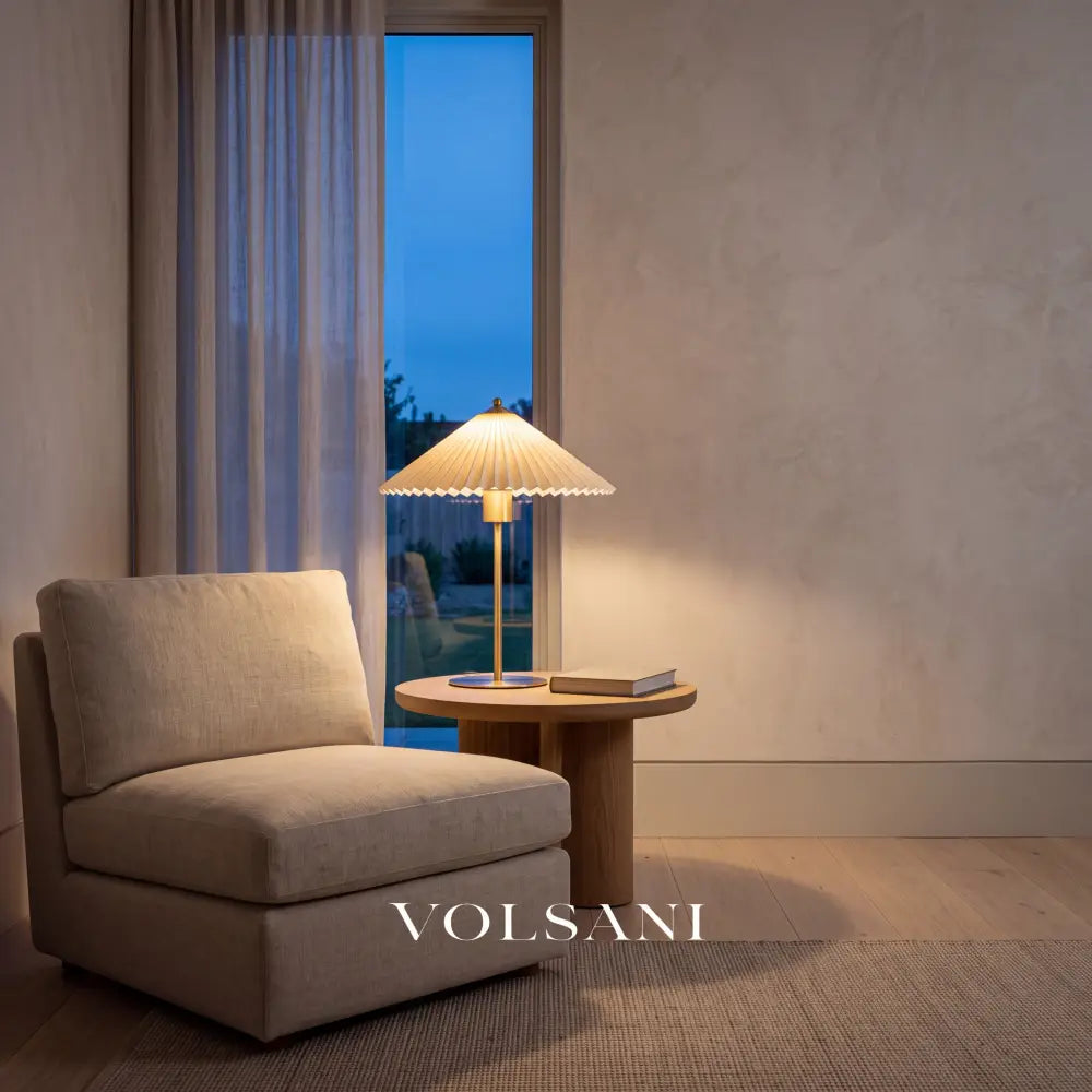 Brushed gold pleated-shade lamp lit in a Japandi reading nook at dusk