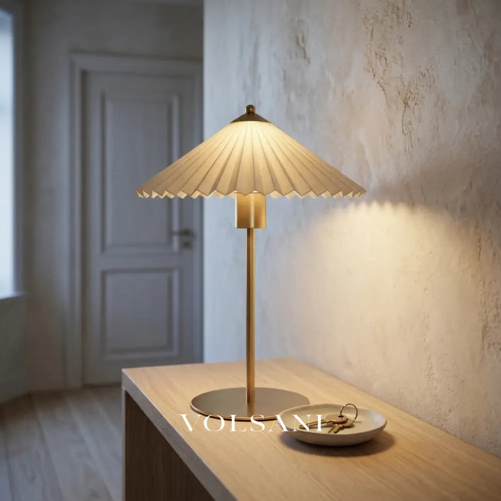 Brushed gold pleated-shade table lamp lit on an oak console at dusk, medium view