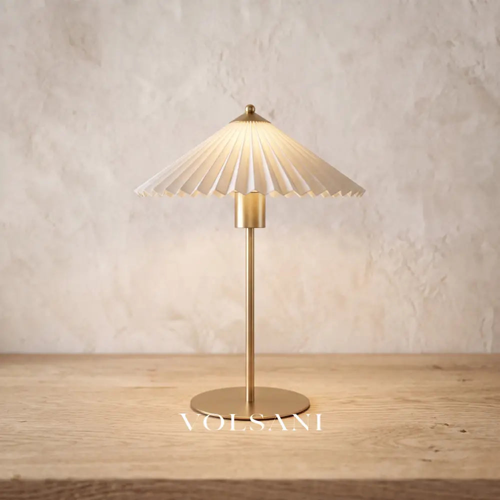 Close-up of the brushed gold pleated-shade lamp on raw oak against a plaster wall