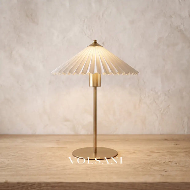 Close-up of the brushed gold pleated-shade lamp on raw oak against a plaster wall