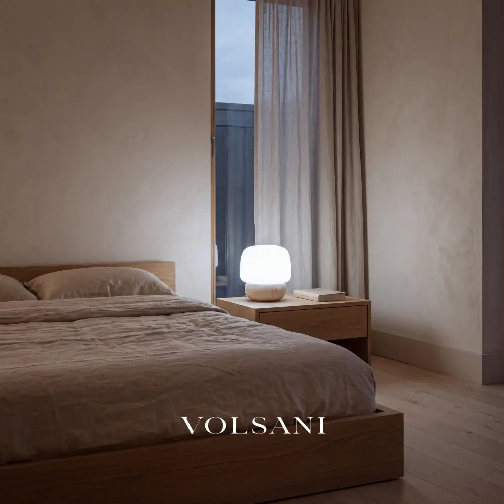 Travertine mushroom lamp lit on a bedside table in a Japandi bedroom at dusk