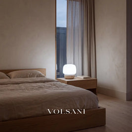 Travertine mushroom lamp lit on a bedside table in a Japandi bedroom at dusk