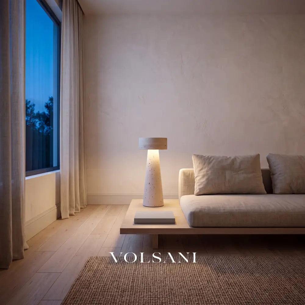 Sculptural travertine lamp lit beside a linen sofa in a Japandi living room at dusk