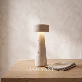 Close-up of the sculptural travertine lamp on raw oak against a plaster wall