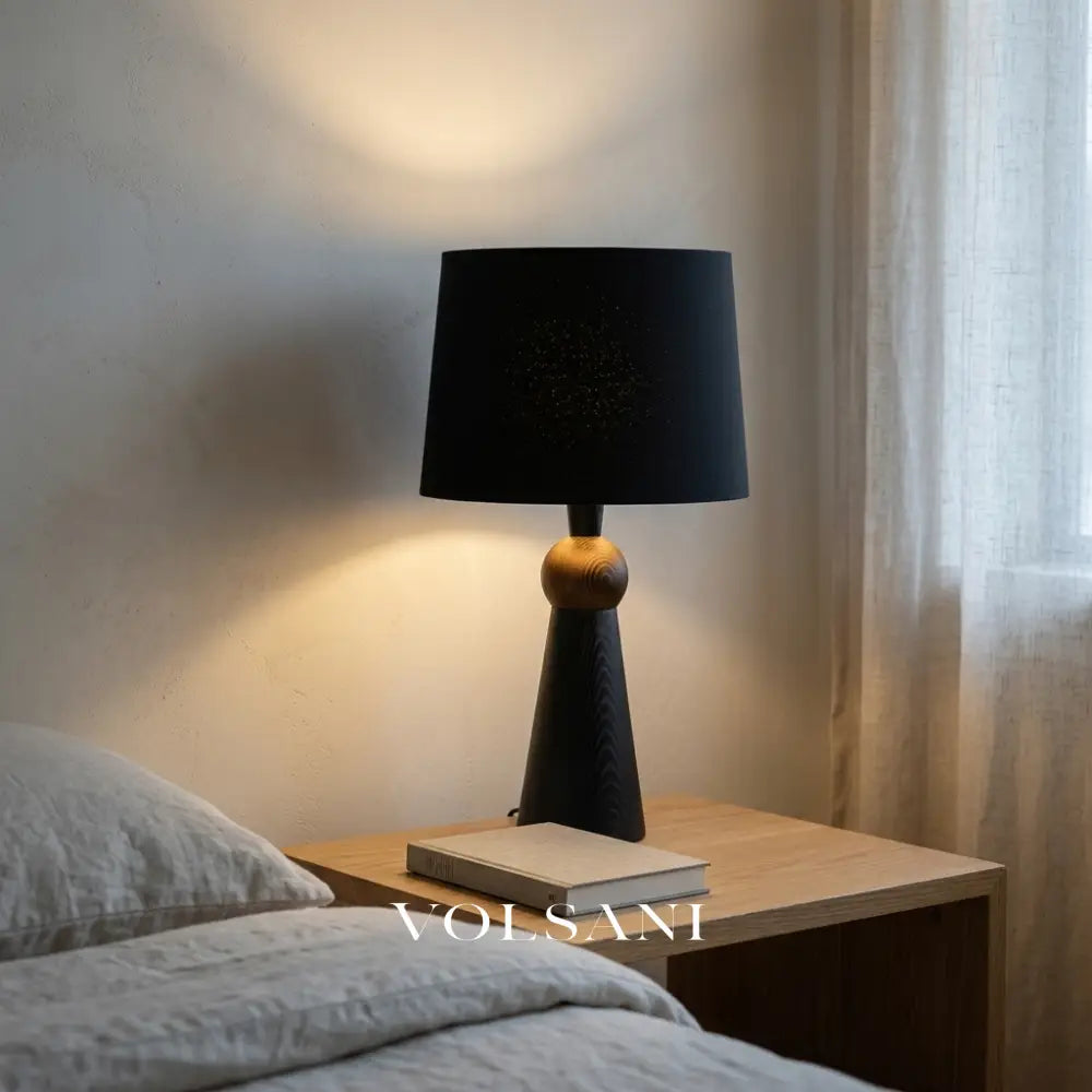 Black-shade Scandinavian wood table lamp lit on a bedside table, medium view